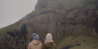 两个时尚的女人走在岛上的后视图。游客看青山，探索冰岛