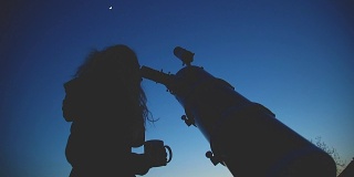 一个女孩的剪影，通过望远镜看星星在自然界。