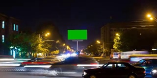 以城市交通为背景的长时间曝光的绿色屏幕广告牌。时间流逝。摄像机移开了