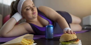 快乐自信的肥胖女孩吃油腻的汉堡而不是运动锻炼