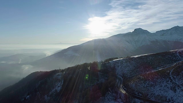 在阳光明媚的日子里，冬季雪山公路的前方鸟瞰图。白色的阿尔卑斯山脉街道小径雪建立与阳光照耀。4k无人机飞行建立镜头