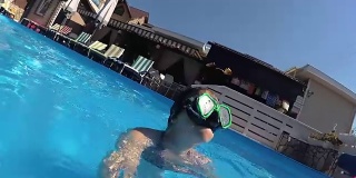 戴着面具的女孩在游泳池里看着镜头，冒着泡泡
