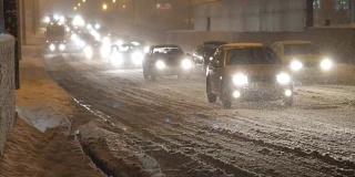 在大雪纷飞的日子里，汽车开着灯在白雪覆盖的路上行驶。