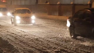 在大雪纷飞的日子里，汽车开着灯在白雪覆盖的路上行驶。视频素材模板下载