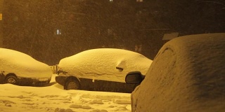 在大雪纷飞的日子里，汽车开着灯在白雪覆盖的路上行驶。