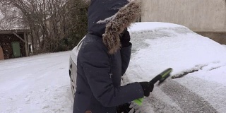 下雪时，女人拿着刷子从车上清除积雪