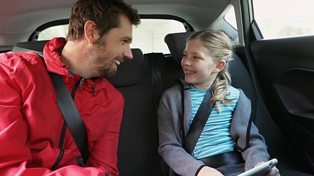 微笑的父亲和女儿用平板电脑坐在车内4K 4K