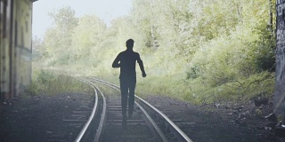 慢镜头男人在铁轨上奔跑的剪影。后视图。抽象背景结束镜头。追求自由