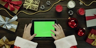 圣诞老人用绿色屏幕的平板电脑被圣诞假期书桌，自上而下拍摄