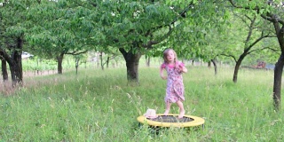 一个可爱的女孩在自然花园里跳舞。小女孩在小蹦床上又跳又跳。小女孩穿着花裙子，戴着白色的帽子。小男孩用弓射箭。低自由度