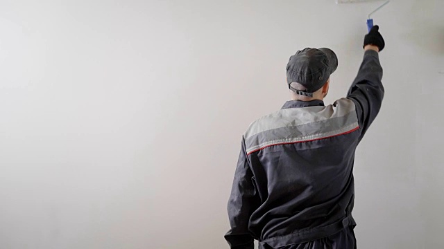 画家站在后面，在一个房间里用油漆滚筒刷墙，工作日