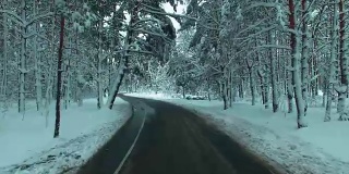 无人机飞过道路穿过冬天的雪林。汽车观点。