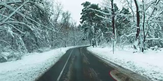 无人机飞过道路穿过冬天的雪林。汽车观点。