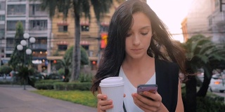 拿着智能手机喝着咖啡在城市里散步的女人，用稳定器拍摄