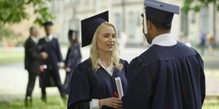 女毕业生戴着方帽拿着毕业证跟同学说话，毕业典礼那天