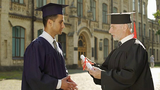 大学校长在毕业典礼上给男同学颁发毕业证书