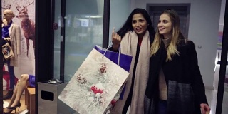 两个可爱的年轻女孩，抱着满满的圣诞礼物，沿着商店的橱窗边逛边欣赏。