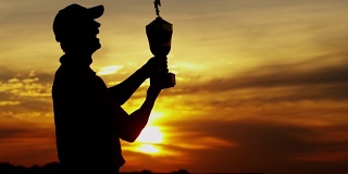 日落剪影成功的男性高尔夫球员持有获奖奖杯