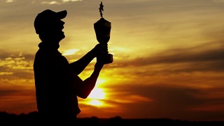 日落剪影成功的男性高尔夫球员持有获奖奖杯视频素材模板下载