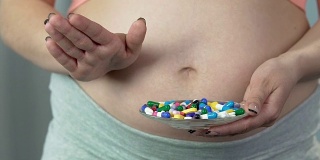 孕妇拿出一碗药丸，做出拒绝的手势，没有药物