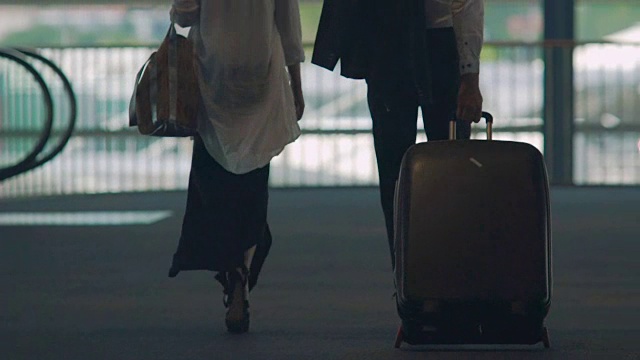 已婚夫妇走过机场天桥，男人提着行李箱，度假