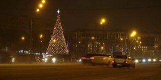 圣诞树在夜晚城市冬天积雪覆盖的道路上闪闪发光，在交通堵塞的车辆中驶过，概念圣诞夜，新年，雪花，吹暴风雪，汽车覆盖的雪，雪花在车灯