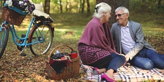 一对浪漫的老夫妇坐在草地上，一边野餐一边放松。