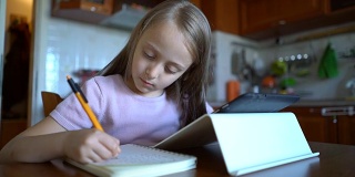 小女孩在笔记本上记笔记，在平板电脑上学习。