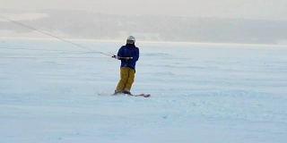 慢动作:一名男运动员正在滑雪板上放风筝。他在一个大湖的冰面上打滚。翻滚时，他会进行各种跳跃、动作和其他练习。雪板上的雪向不同的方向飞舞。