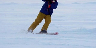 慢动作:一名男运动员正在滑雪板上放风筝。他在一个大湖的冰面上打滚。翻滚时，他会进行各种跳跃、动作和其他练习。雪板上的雪向不同的方向飞舞。