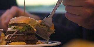 男人切着汉堡吃，快餐和肥胖，特写