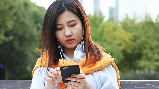 4K:美丽的亚洲女人在中国上海的公园里听着音乐