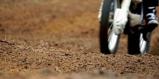 慢动作:运动摩托车车轮的特写视频。摩托车在一条不平的土路上行驶。这些粘土碎片散落在不同的方向。多云的秋天懒惰。