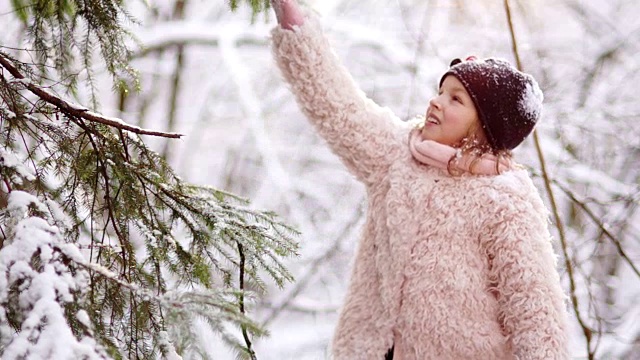 一个可爱的女孩摇着冬天树上的雪。冬季游戏，节日快乐，圣诞假期