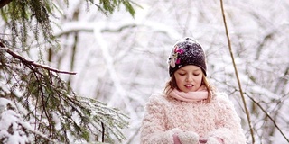 快乐的女孩在森林里摇着树枝上的雪。快乐的童年。冬天的乐趣