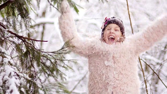 冬天的森林里，一个美丽的女孩在雪地里快乐。她穿着一件粉红色的外套，戴着手套和一顶黑色的帽子