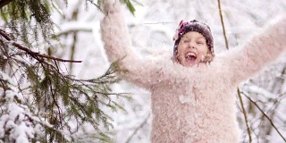 冬天的森林里，一个美丽的女孩在雪地里快乐。她穿着一件粉红色的外套，戴着手套和一顶黑色的帽子