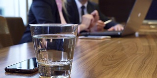 一张桌子上放着一杯水和一部iPhone的特写