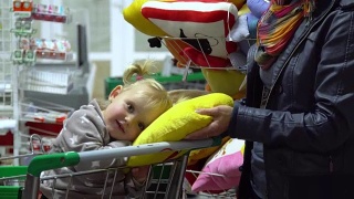 一位带着孩子的年轻妇女在超市选购商品。妈妈正用手推车载着一个小女孩。妈妈和女儿在看枕头。视频素材模板下载