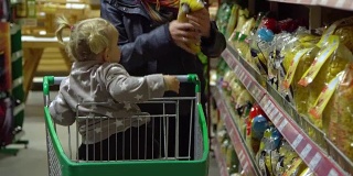 一位带着孩子的年轻妇女在超市选购商品。妈妈正用手推车载着一个小女孩。妈妈和女儿选择食物。