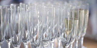 在庆祝活动中，优雅的玻璃杯和香槟酒排成一排摆放在餐桌上。服务员倒香槟