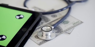 4k视频的听诊器与金钱和平板电脑在绿色屏幕上。保健概念