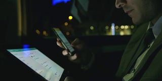 晚上在出租车上使用智能手机和平板电脑的商人