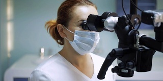 女牙医使用牙科工具-显微镜，镜子和探针在牙科诊所治疗病人的牙齿。医学、牙科和保健概念。牙科设备