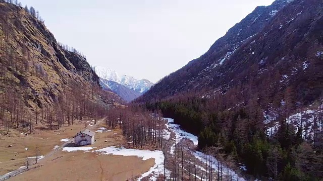 空中飞行向后移动，远离黄山沟附近的小木屋和森林森林，落建物。秋冬户外雪野自然景观。4k无人机飞行建立