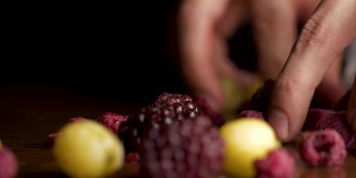 男性的手拿着浆果和木桌在黑色的背景。男性手拿黑莓、蔓越莓、加仑子、醋栗、沙棘等浆果落在黑色的背景上
