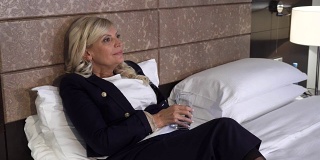 一位优雅的女子躺在酒店房间的沙发上喝水