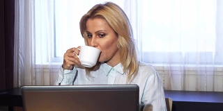 商务女士坐在笔记本电脑前喝咖啡