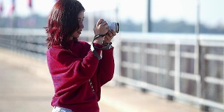 年轻的亚洲女孩与红裙抓住和拍照在大坝上