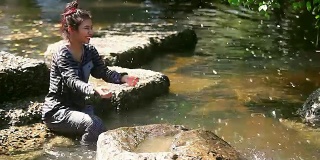 小女孩坐在小溪边，独自捡起水玩
